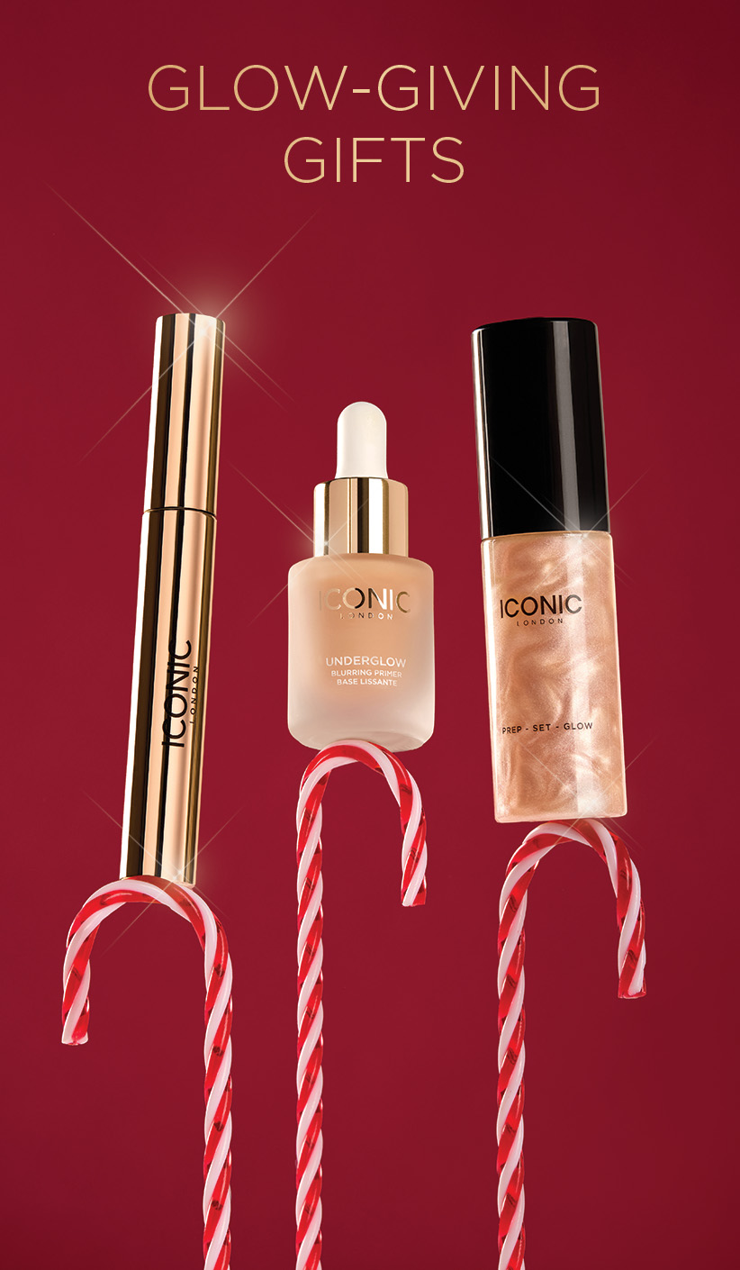 Three Iconic London makeup products, including primer and setting spray, balanced on candy canes against a red background.
