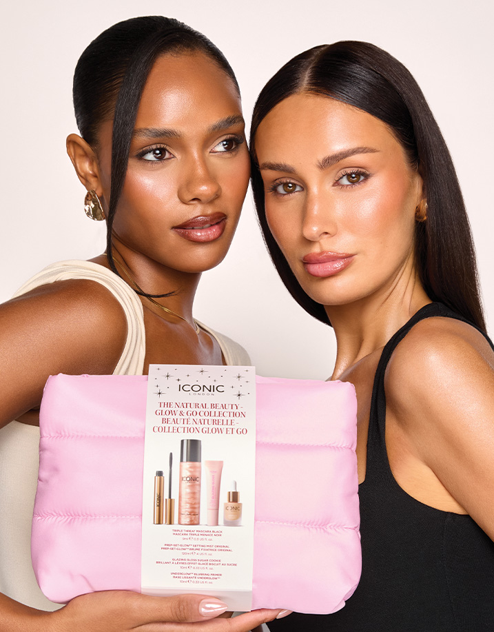 Two women with glowing makeup hold a pink quilted bag with an ICONIC LONDON makeup set.