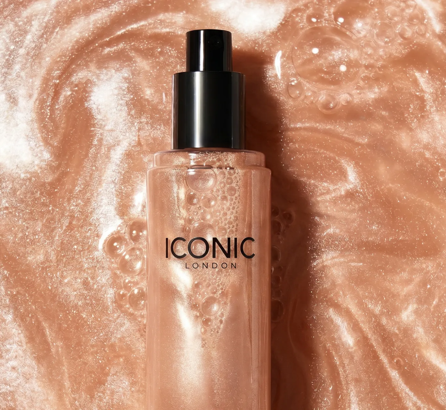 A bottle of Iconic London product lies in a swirling, shimmery, bubbly rose-gold liquid.