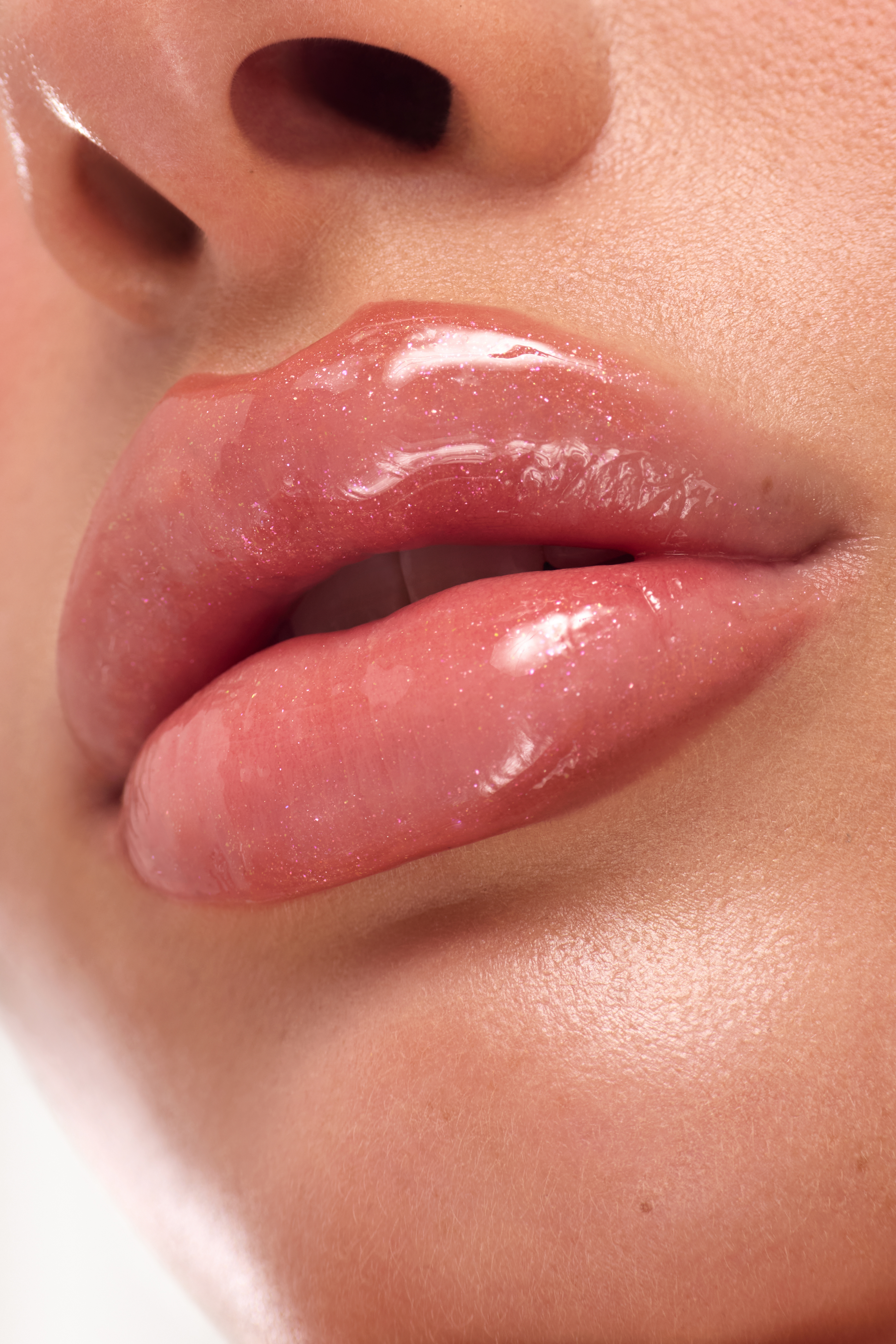 A close-up of a person's mouth with glossy, sparkly pink lip gloss applied to their full lips.