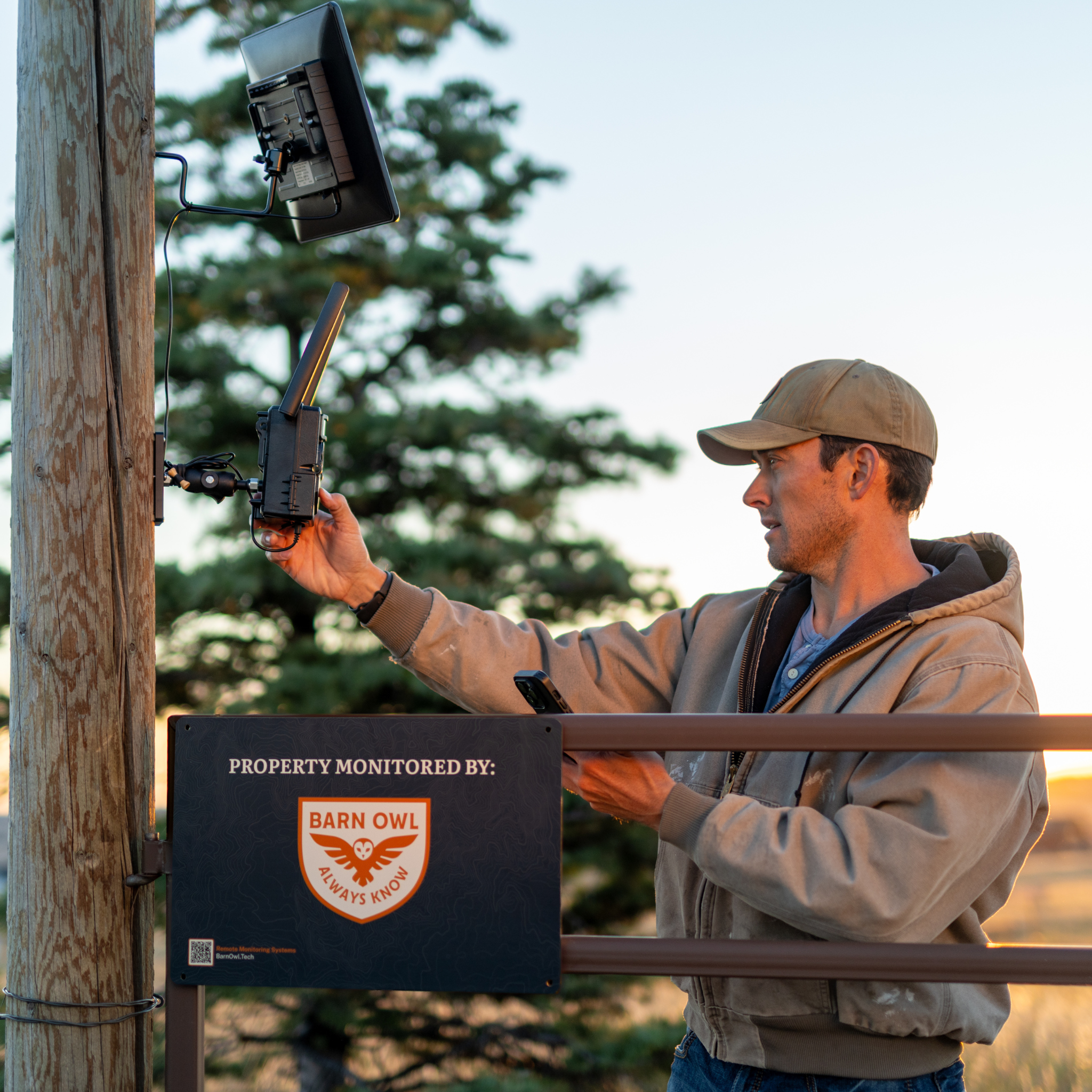 Person adjusting a security camera on a wooden post with a monitoring sign.