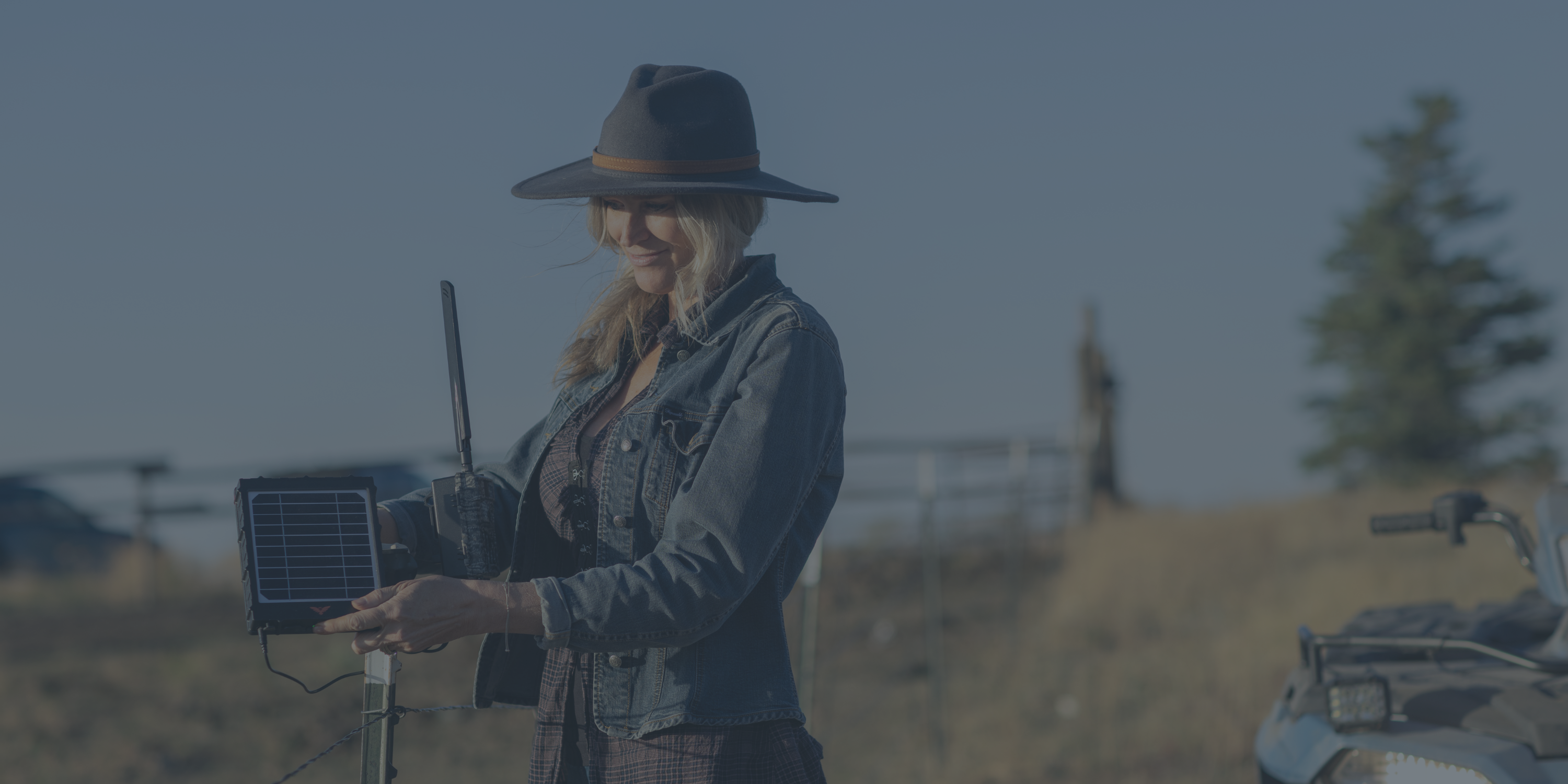 Person in a hat adjusting a solar-powered device on a fence.
