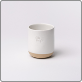 A white ceramic cup with a tan base and embossed lettering, set against a plain background.