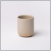 A light beige, handleless ceramic cup with a raw clay base, on a white background.