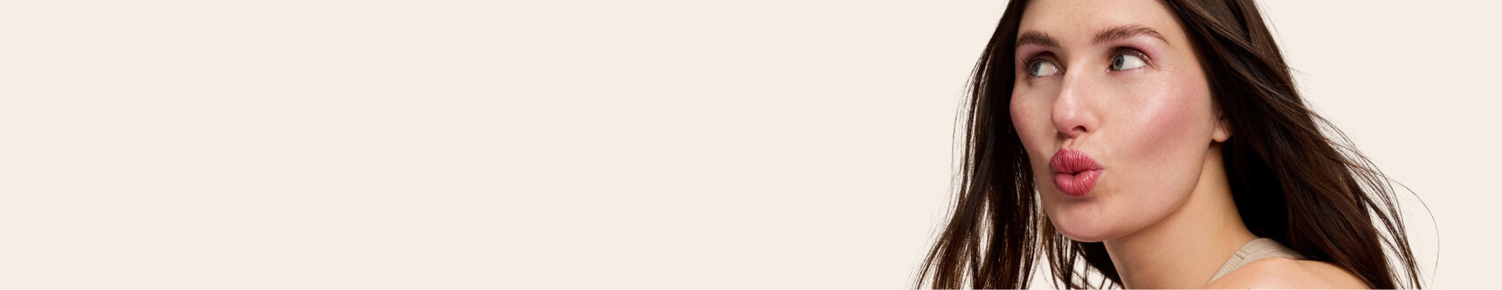 Woman with long hair making a playful face against a plain background.