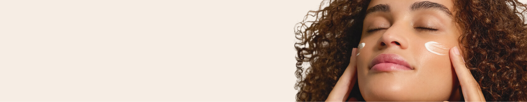 Person applying cream to their face with closed eyes.