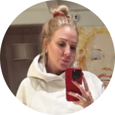 A woman with blonde hair in a bun takes a mirror selfie with a red phone.