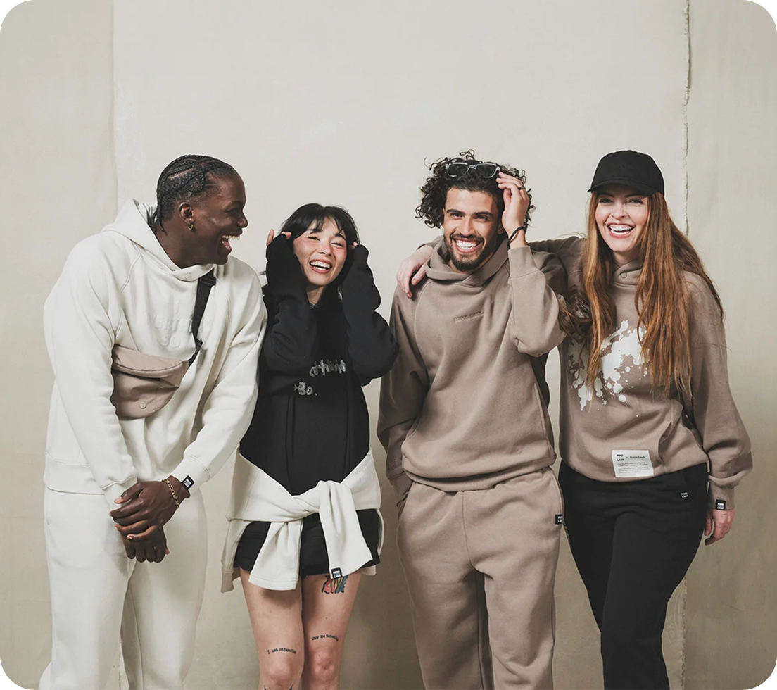 A diverse group of four people laughing and posing together in casual hoodies and sweatpants.