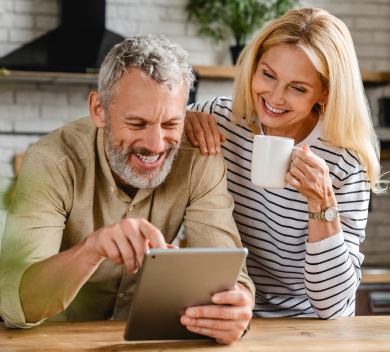 Smiling man and woman looking at a tablet, woman holding a mug.