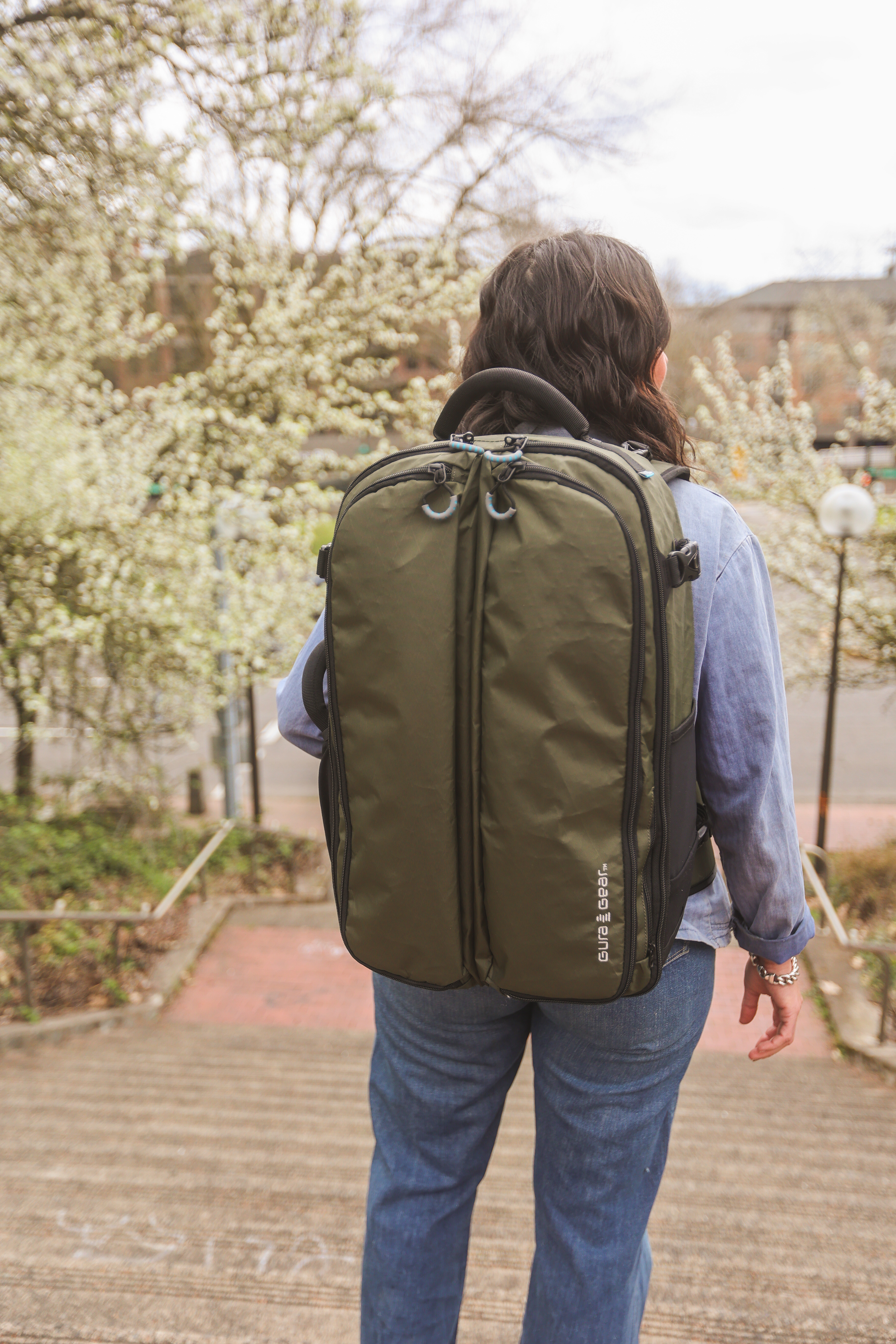 A person seen from behind wearing an olive green backpack stands at the top of outdoor stairs.