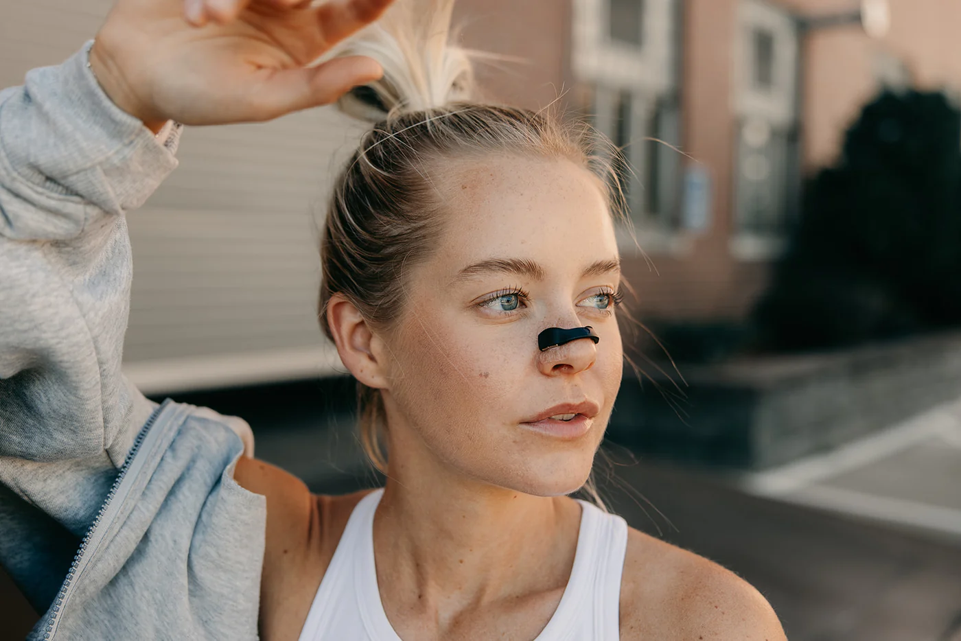 Woman with a nose strip, wearing a tank top, outdoors.