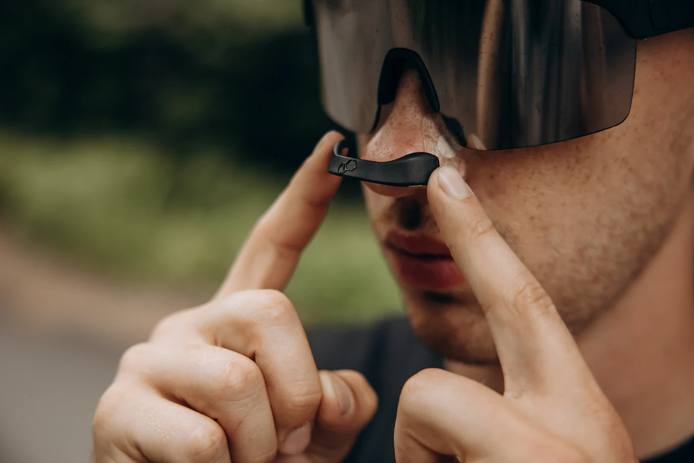 Person adjusting nose piece of large sunglasses outdoors.