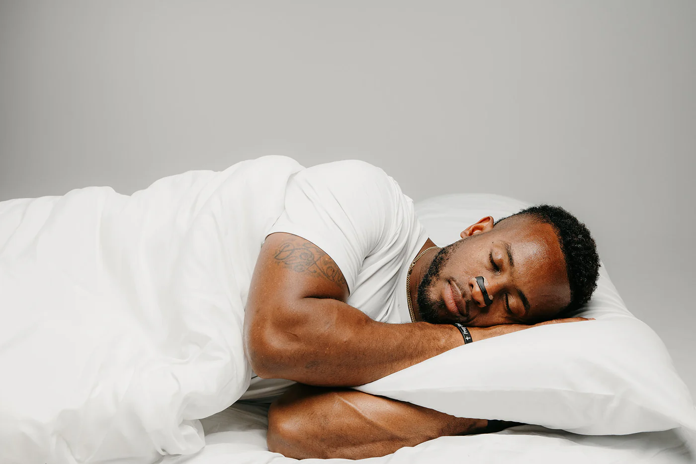 Man sleeping on white bed with a nasal strip.
