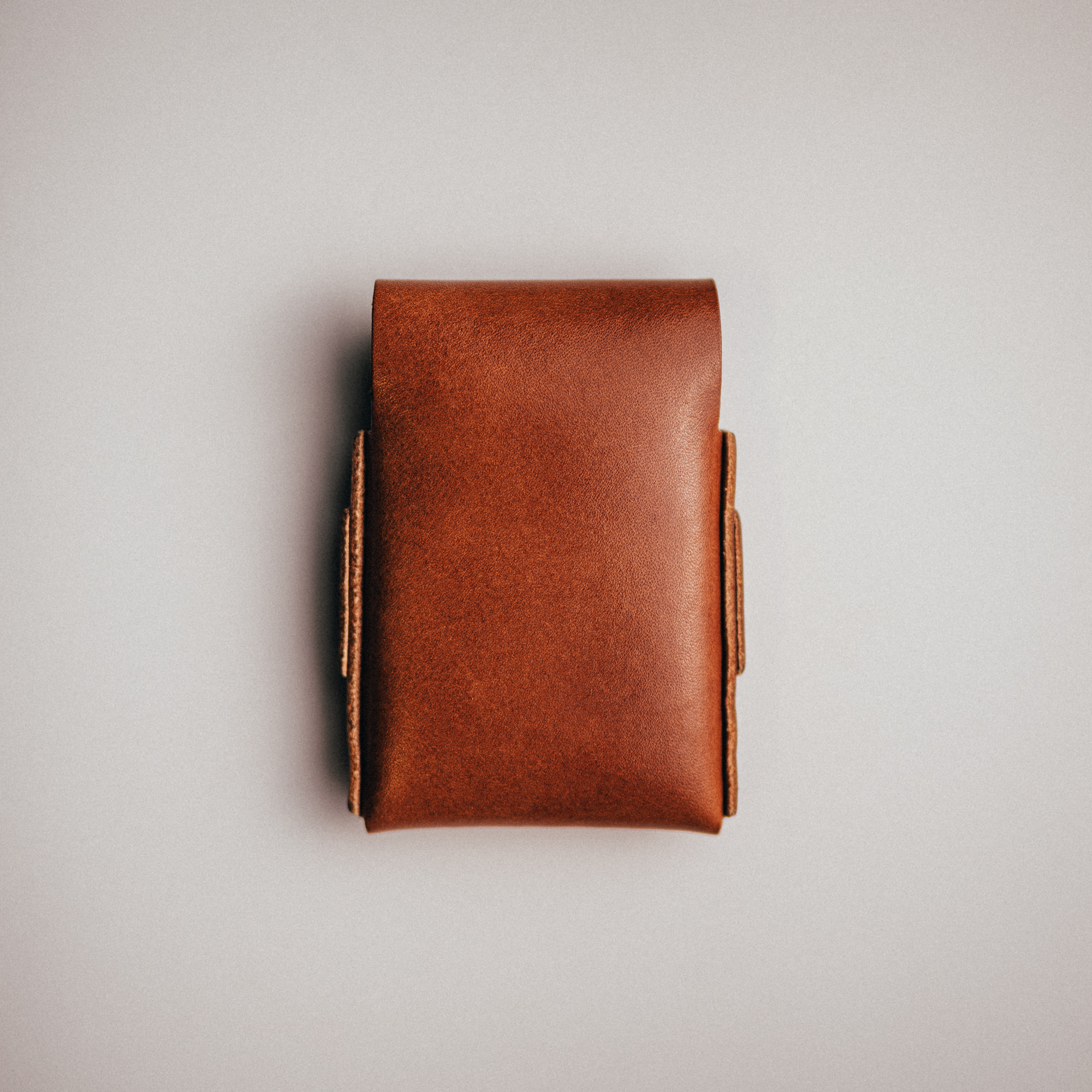 A top-down view of a small brown leather pouch lying on a plain gray surface.