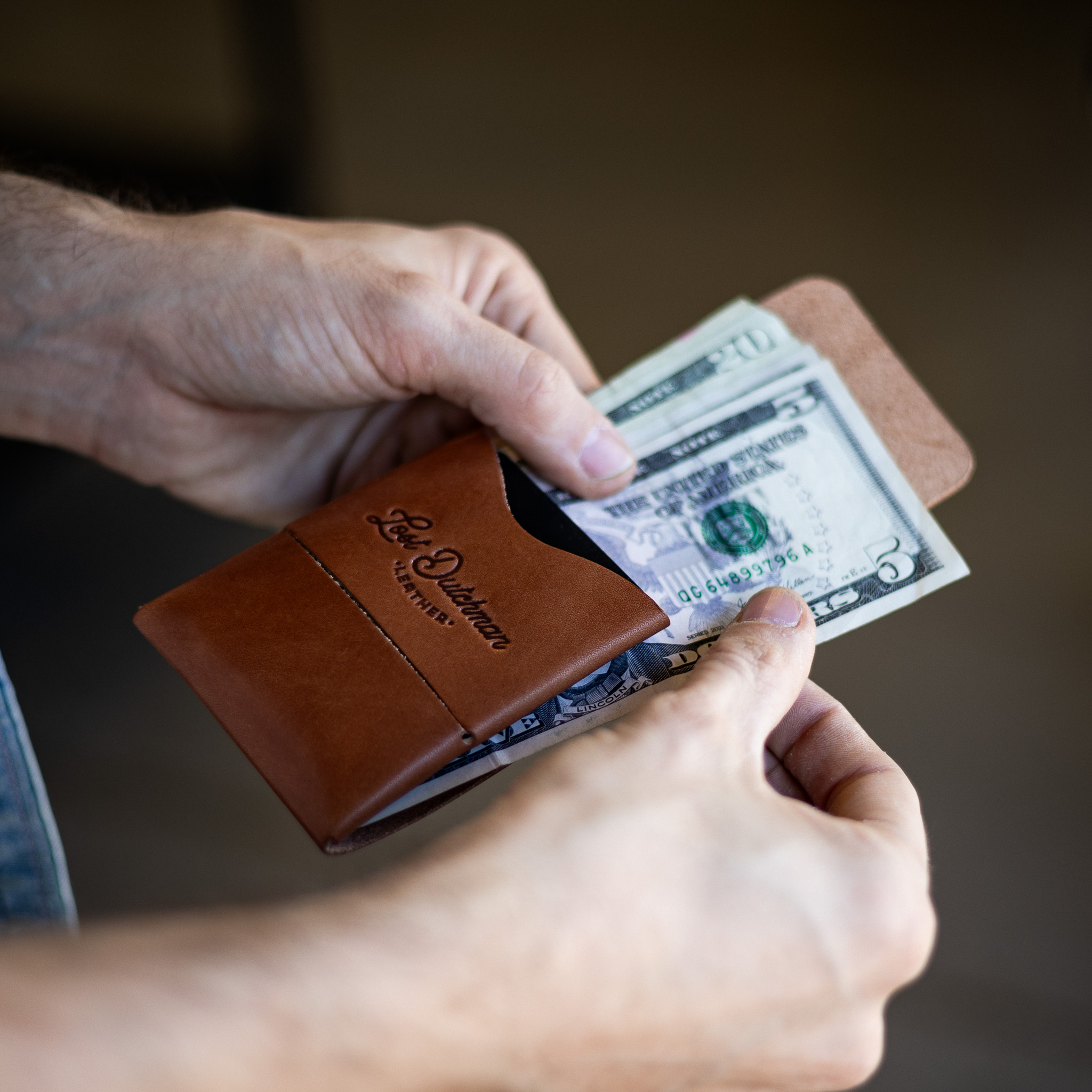 A pair of hands holding a brown leather wallet with several US dollar bills.