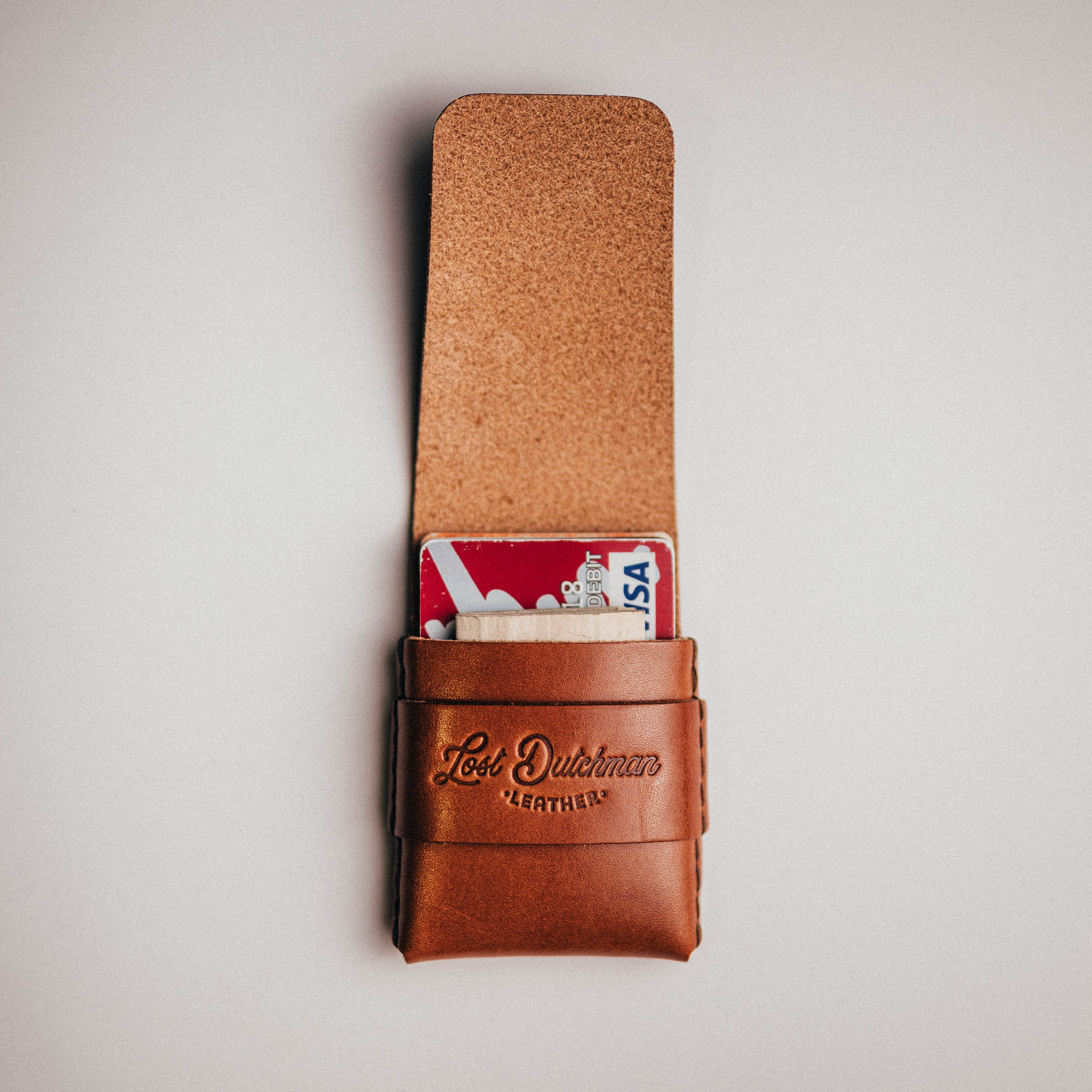 An open brown leather cardholder from Lost Dutchman Leather with a credit card peeking out.
