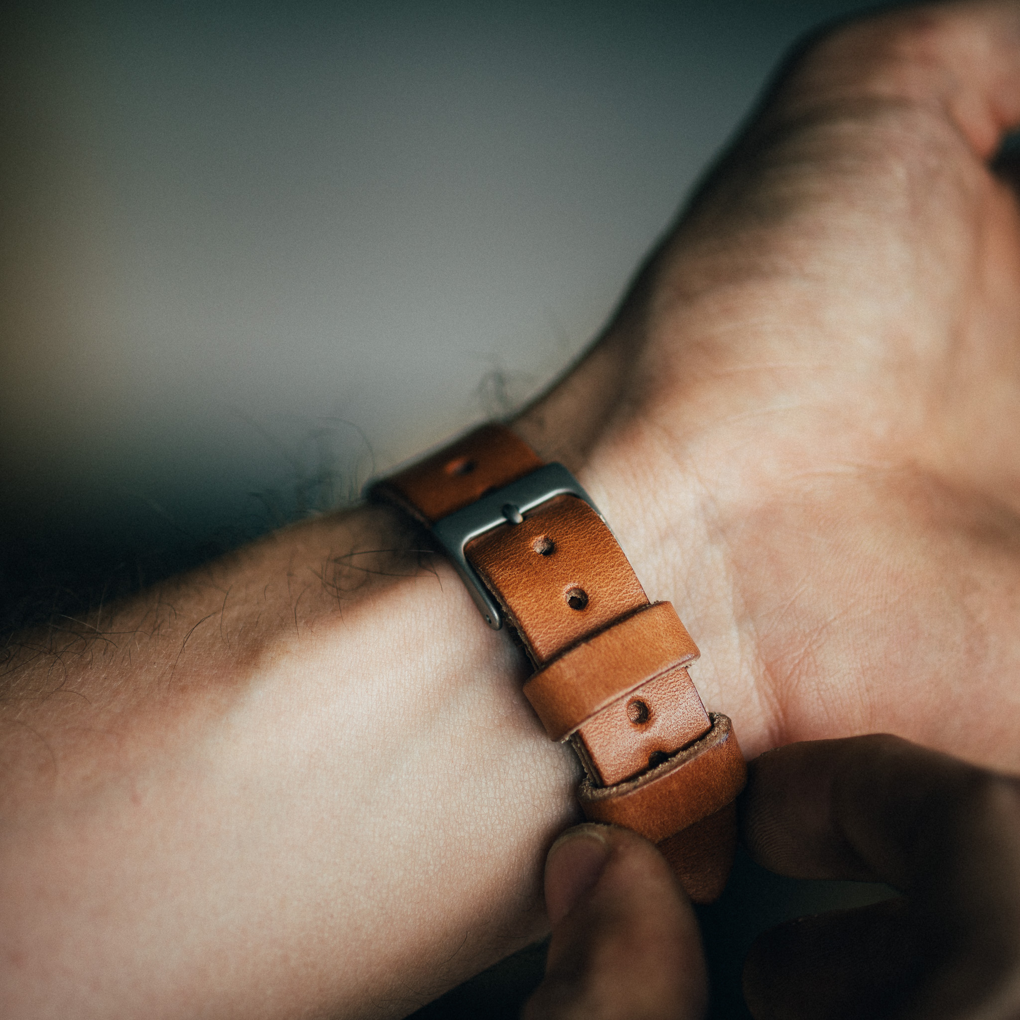 A person adjusts a brown leather watch strap on their wrist in a close-up shot.