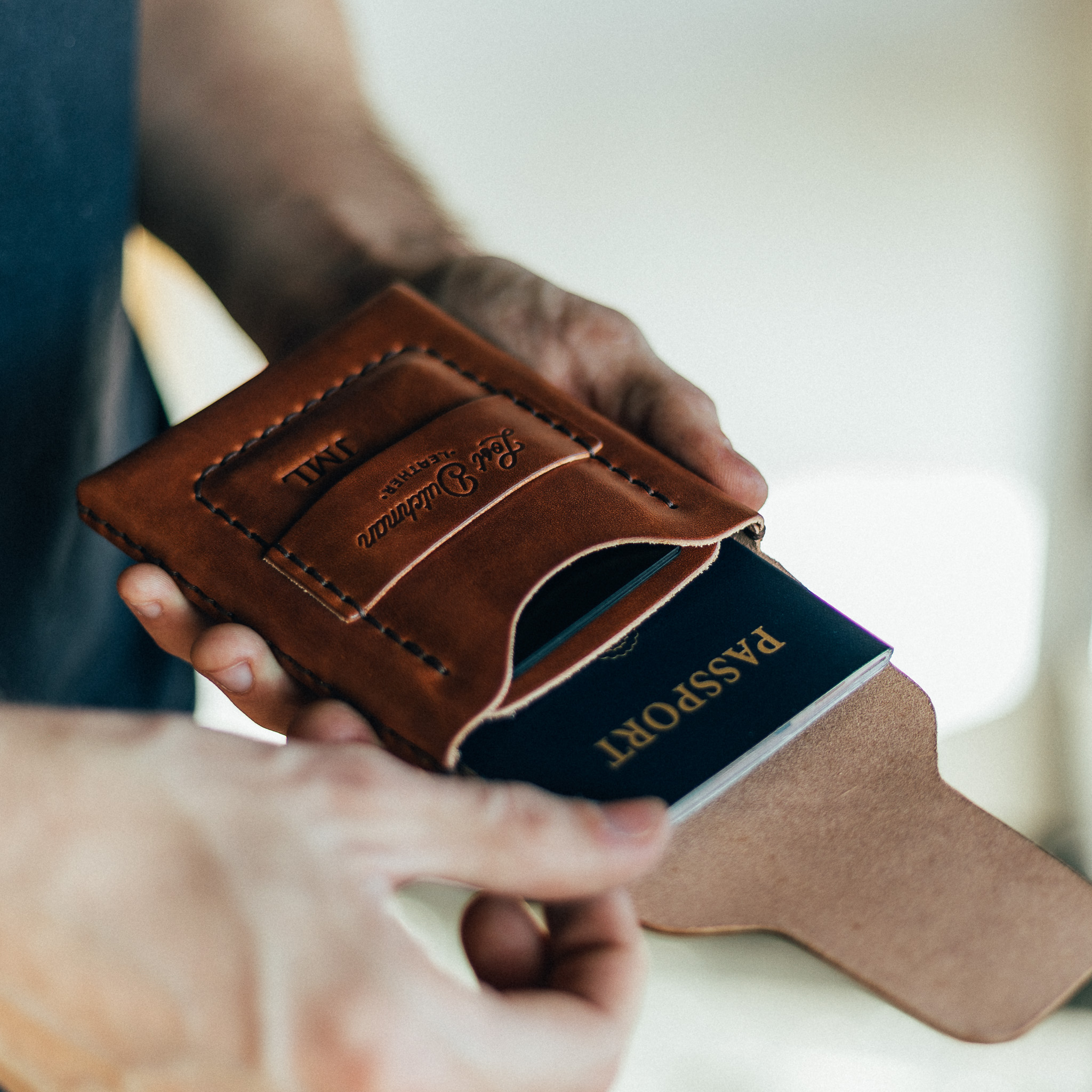 A person places a dark blue passport into a brown leather passport holder.