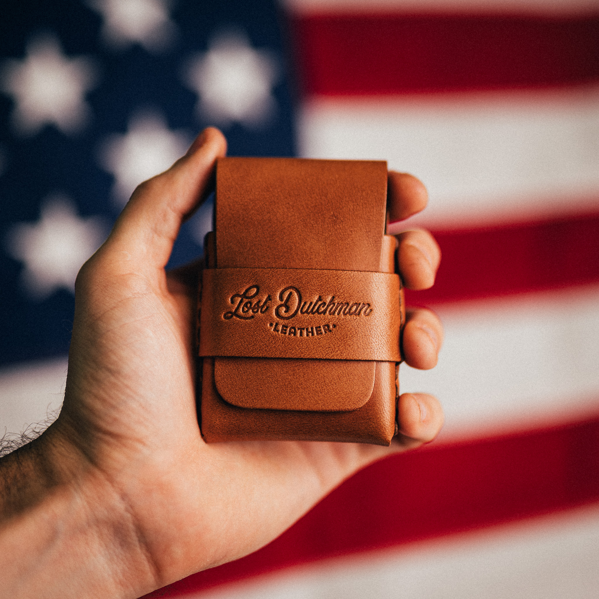 A hand holds a brown leather wallet with an American flag in the background.