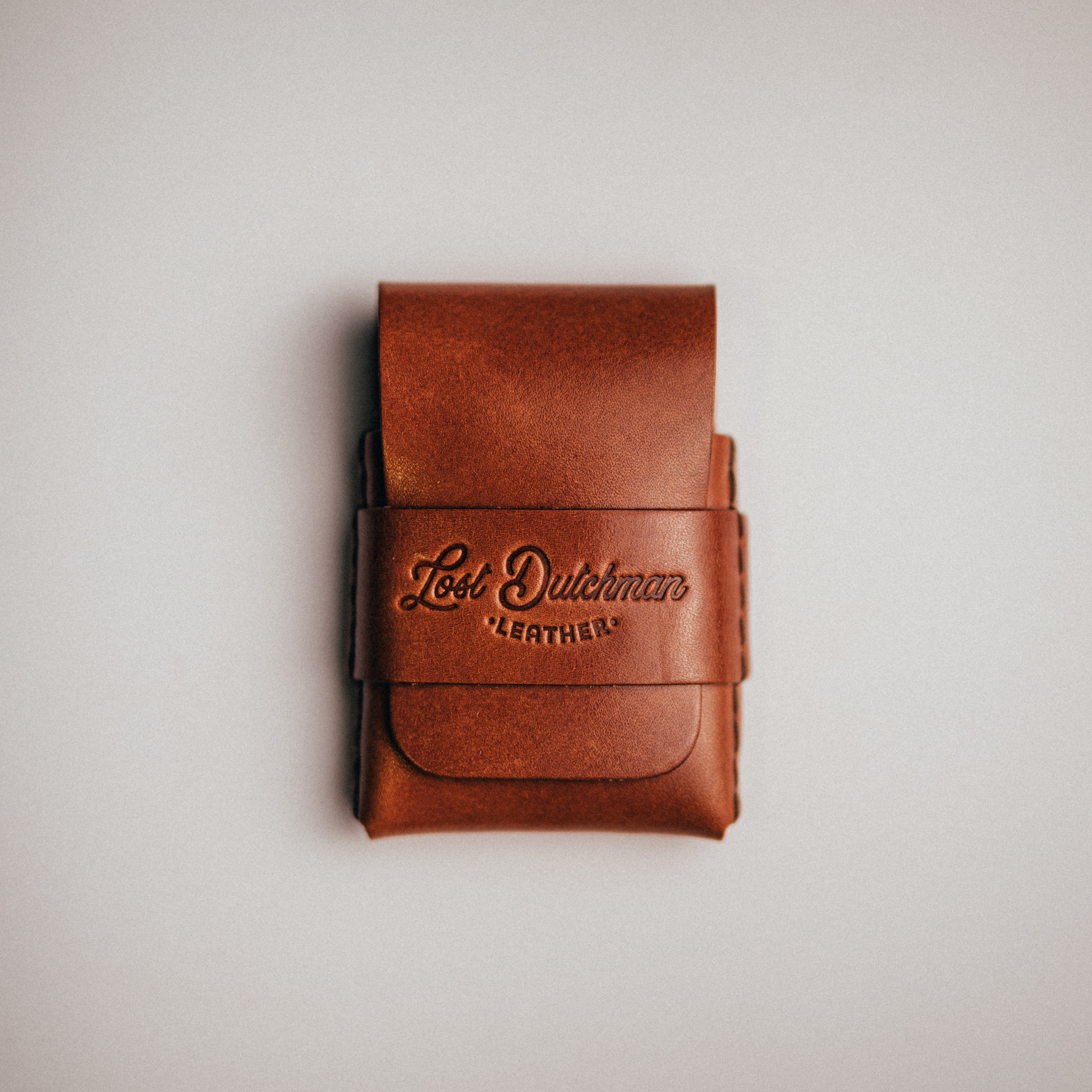 A brown leather wallet with the 'Lost Dutchman Leather' logo, shot from above on a plain background.