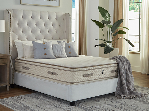 A mattress on a bed with a tufted headboard, pillows, and throw in a decorated bedroom.