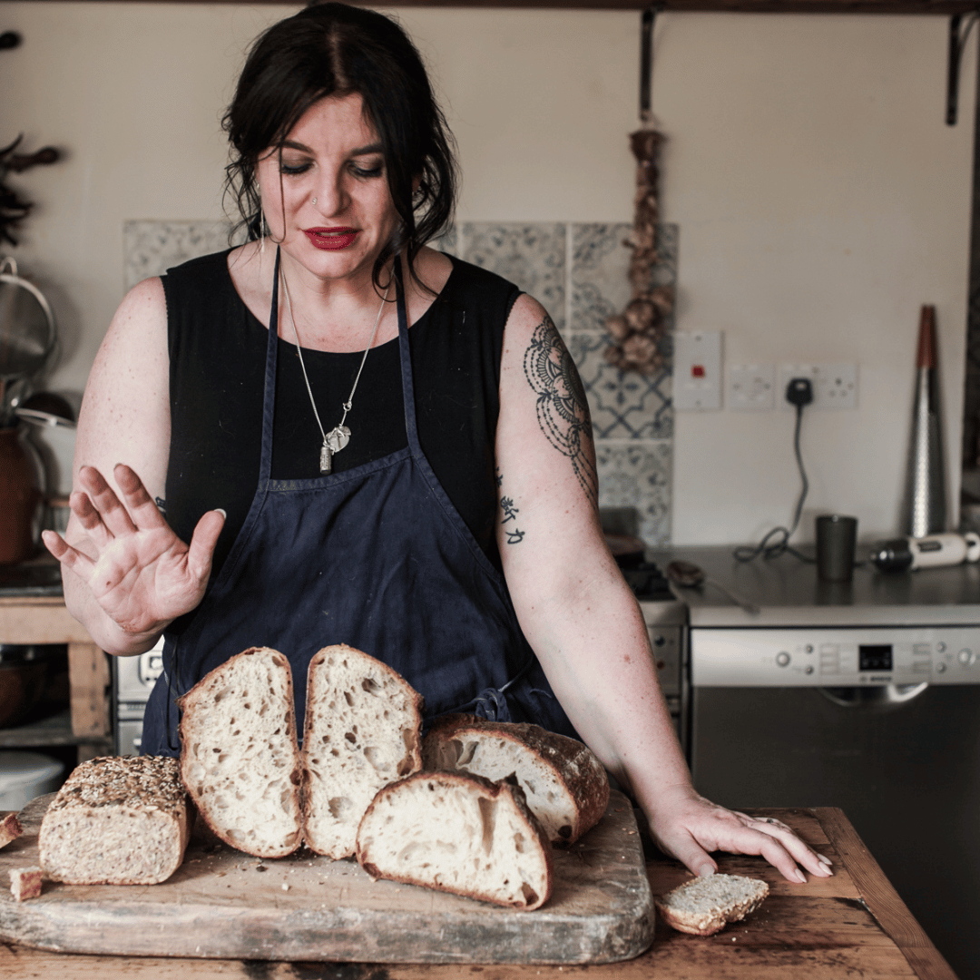 Person in apron with sliced bread on a wooden board in a kitchen.