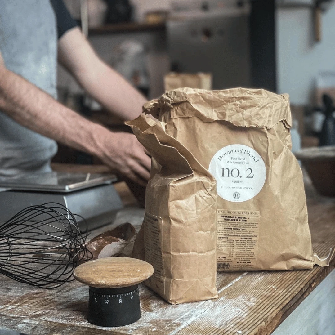 Bags of flour, a whisk, and a scale on a wooden kitchen counter.