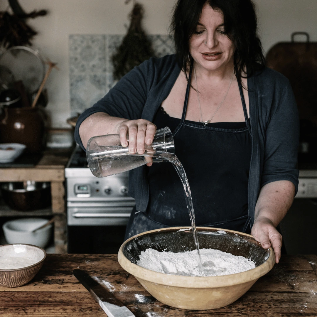 Person pouring water into a bowl of flour in a kitchen.