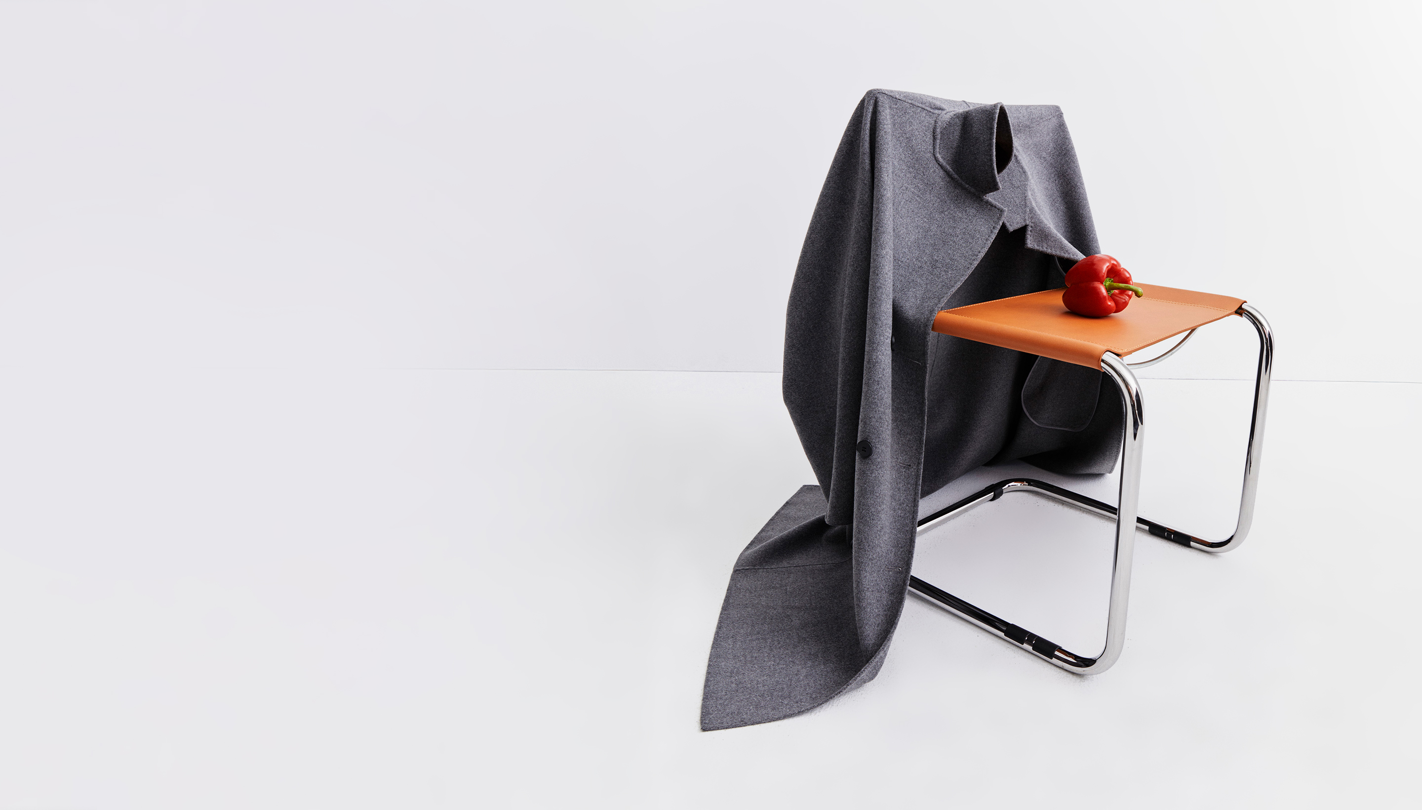 A gray coat draped over a chair with a red bell pepper on the seat.