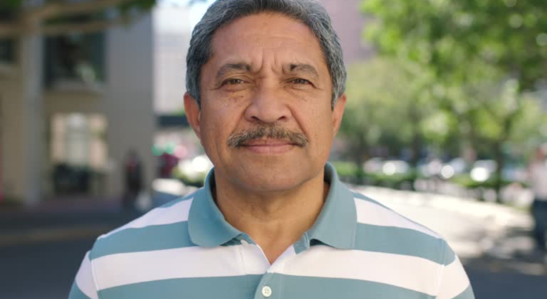 Man in a striped shirt standing outdoors with trees in the background.