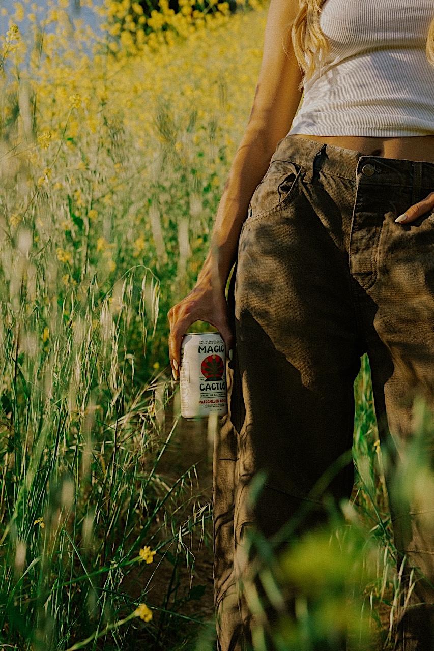 Hand holding a can of Magic Cactus in a grassy field