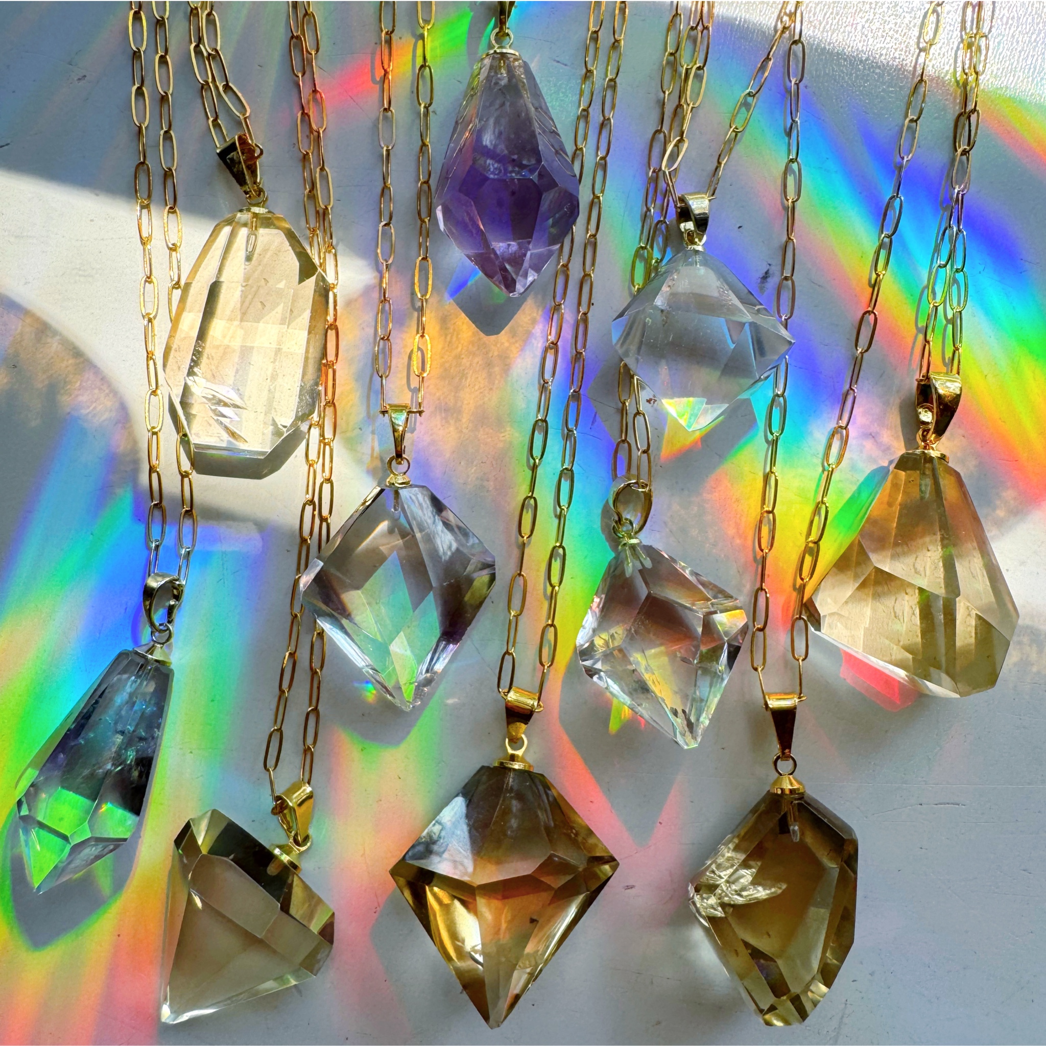Faceted crystal pendants on gold chains with rainbow light reflections.