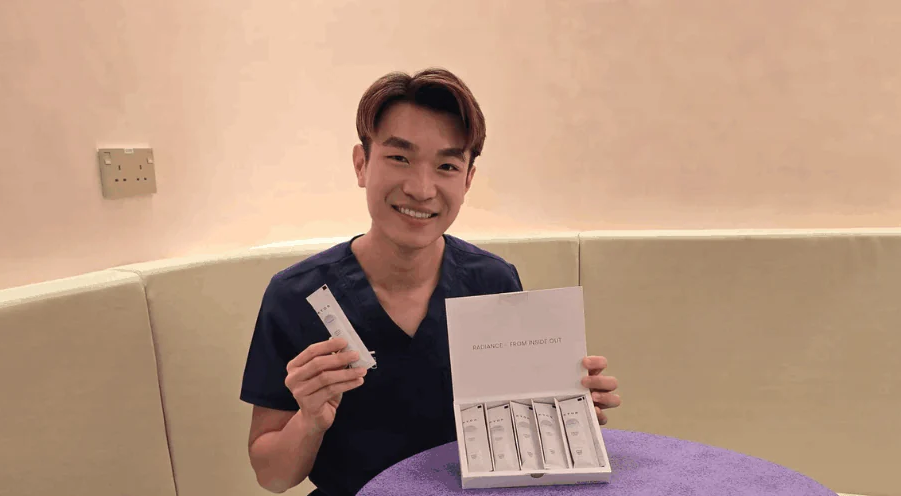 A smiling man in a dark shirt holds an open box and a single packet of a product.