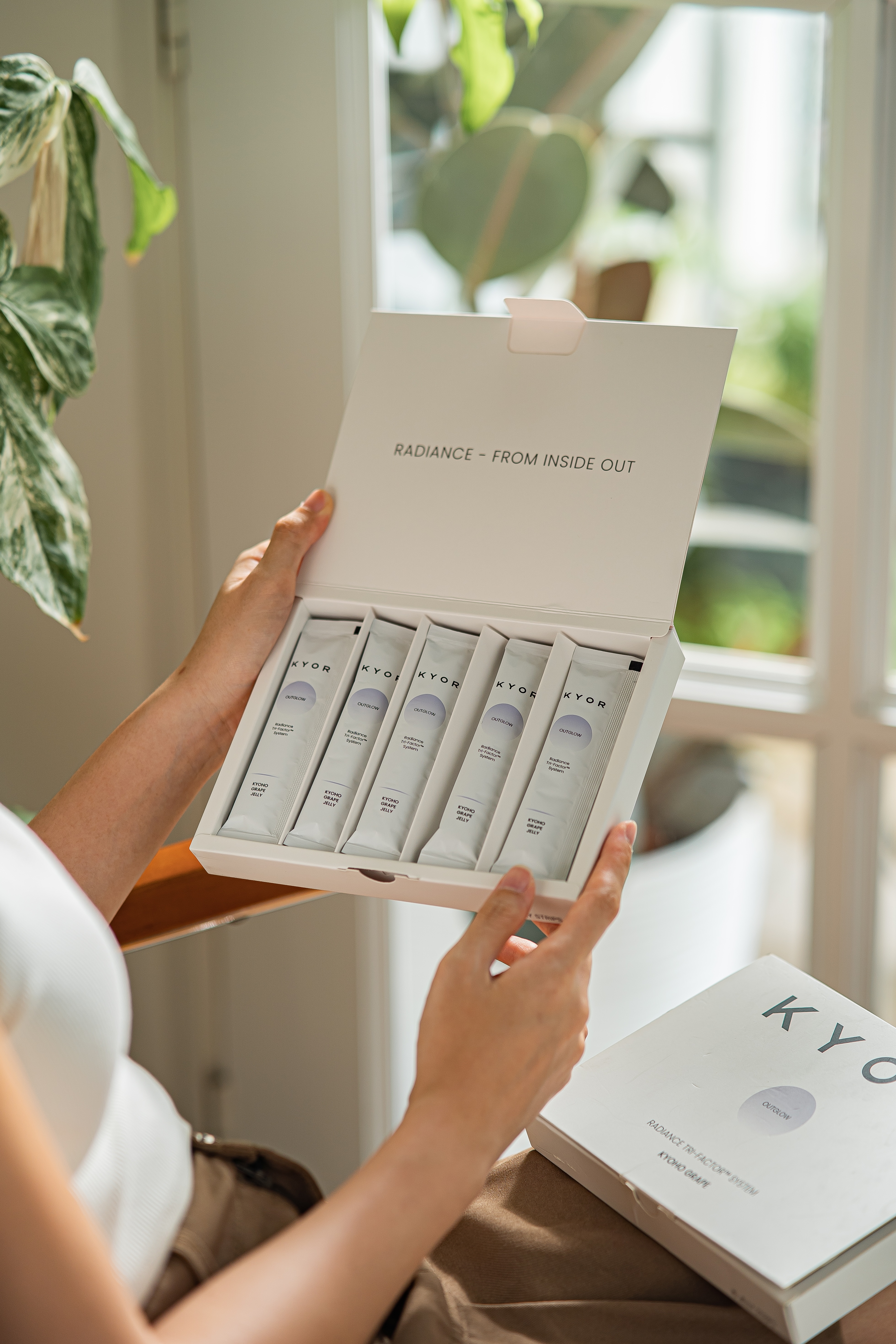 A person holds open a white box containing several individual sachets of a KYOR wellness product.