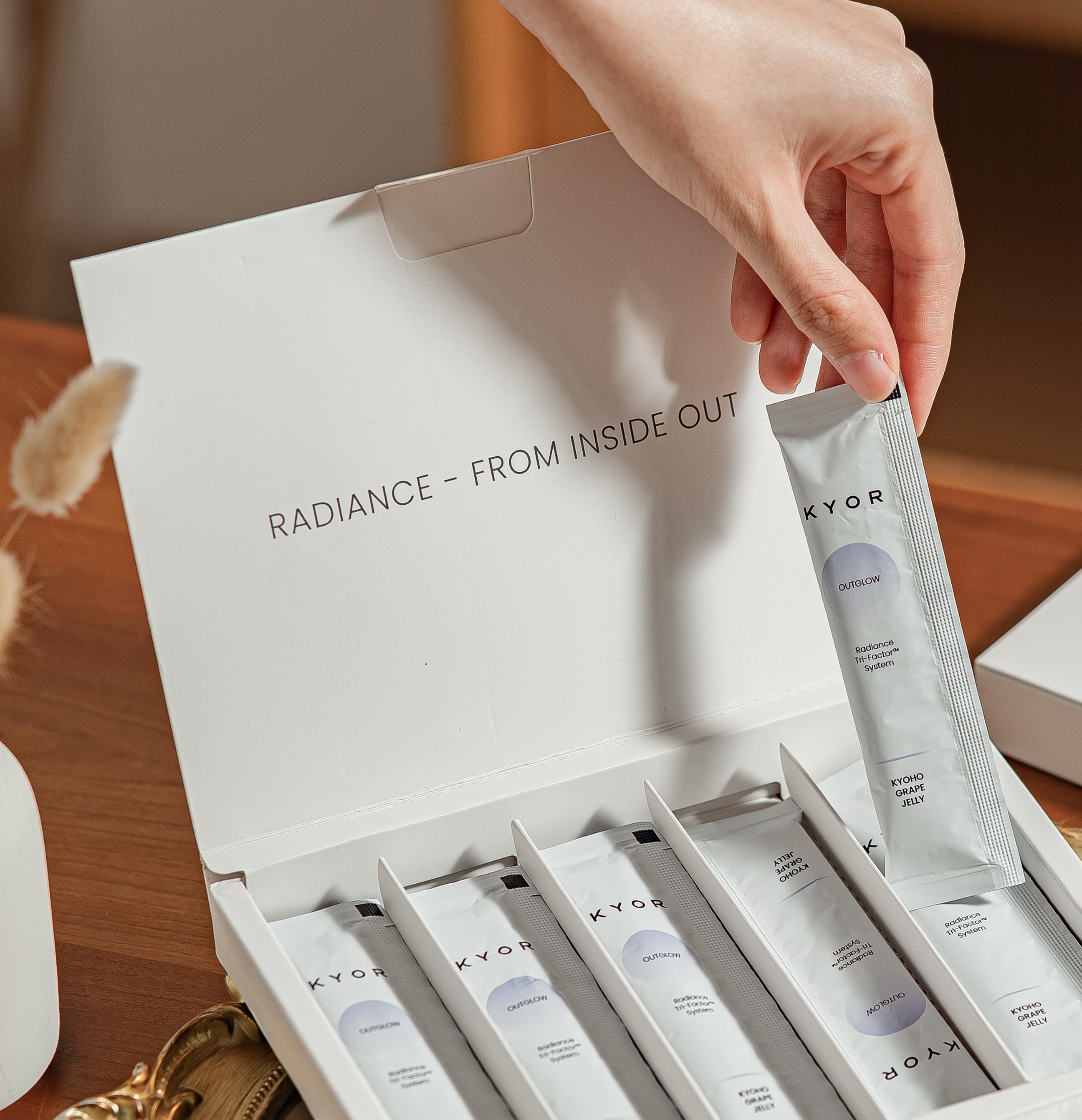 A hand taking a single-serving sachet of a KYOR beauty product out of an open box.