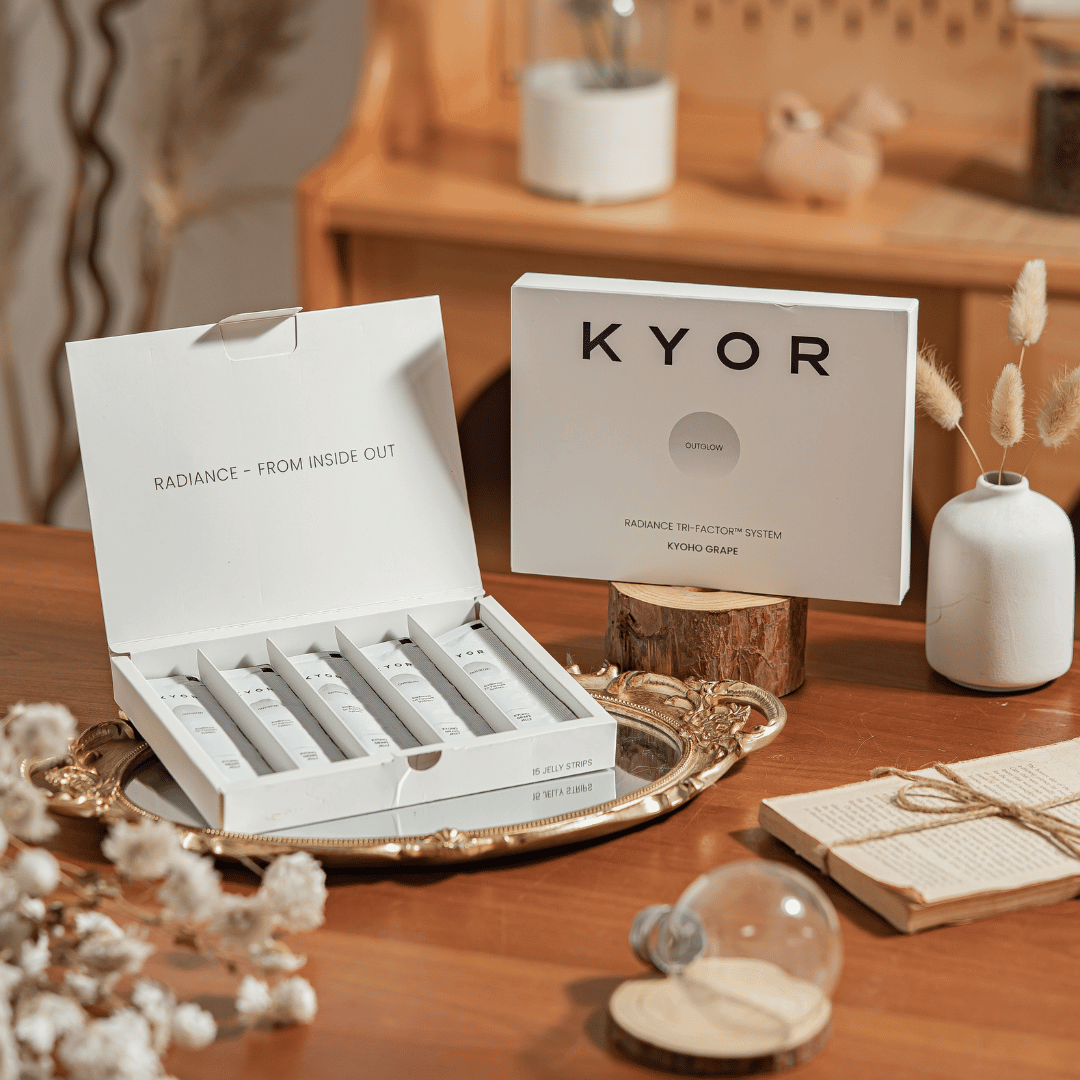 Two white boxes of KYOR Radiance Tri-Factor System on a styled wooden table with decorative items.
