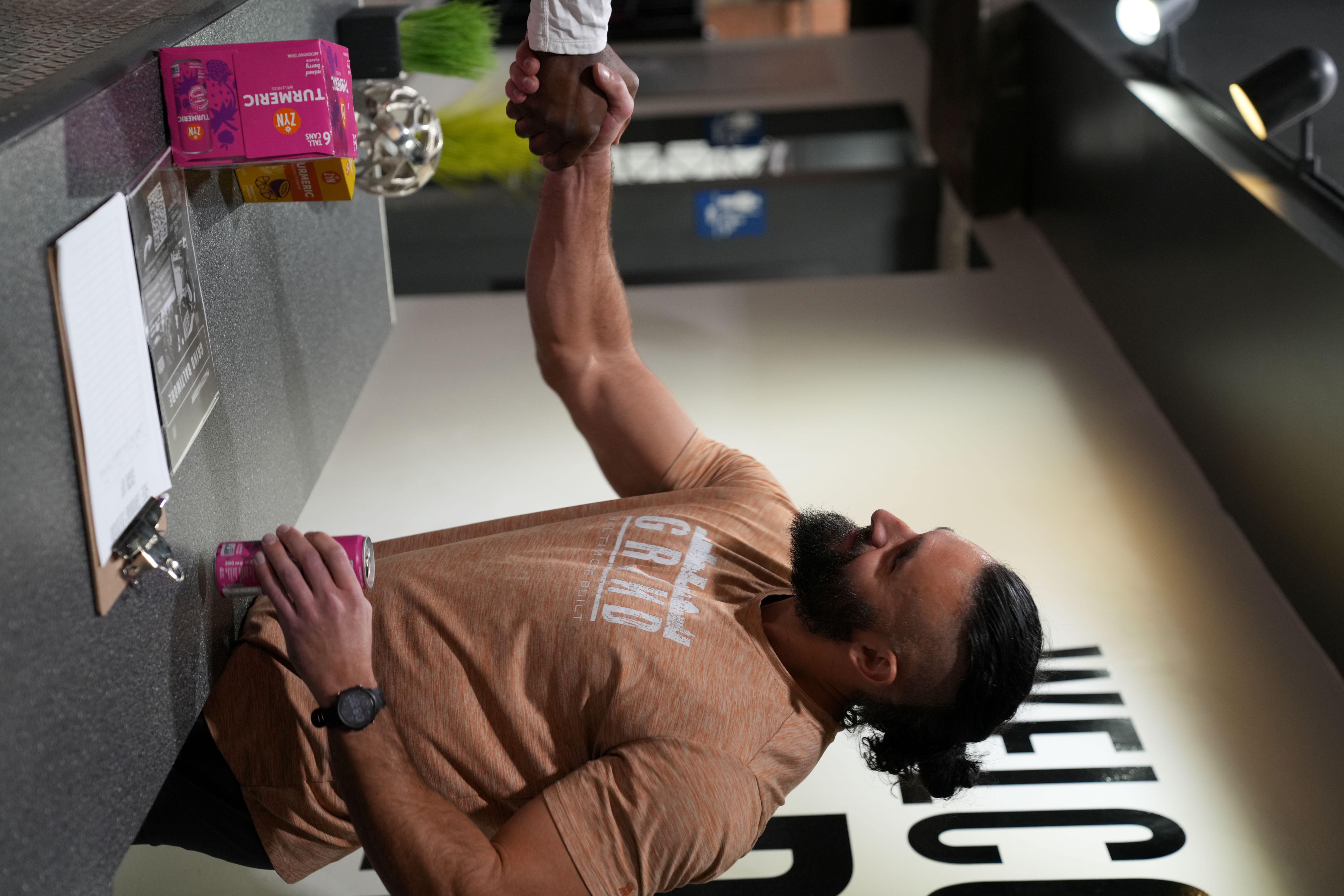 Two people shaking hands at a counter with drinks and a clipboard.