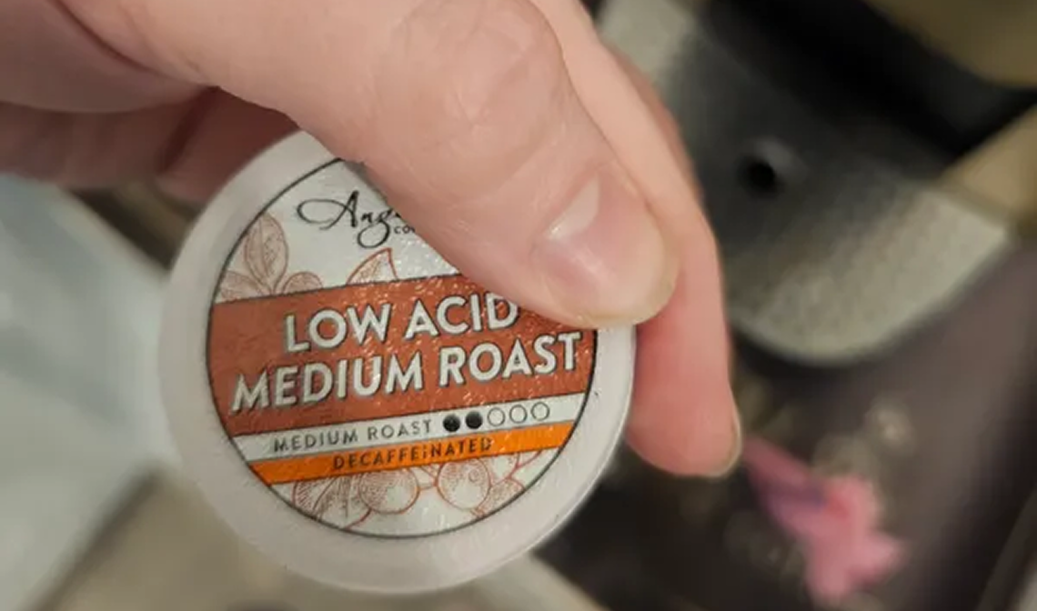Hand holding a coffee pod labeled 'Low Acid Medium Roast.'