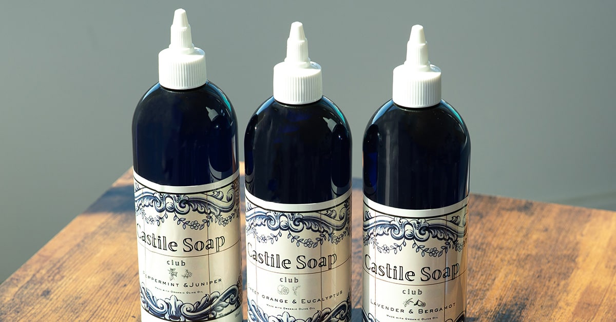 Three bottles of Castile soap with decorative labels on a wooden surface.