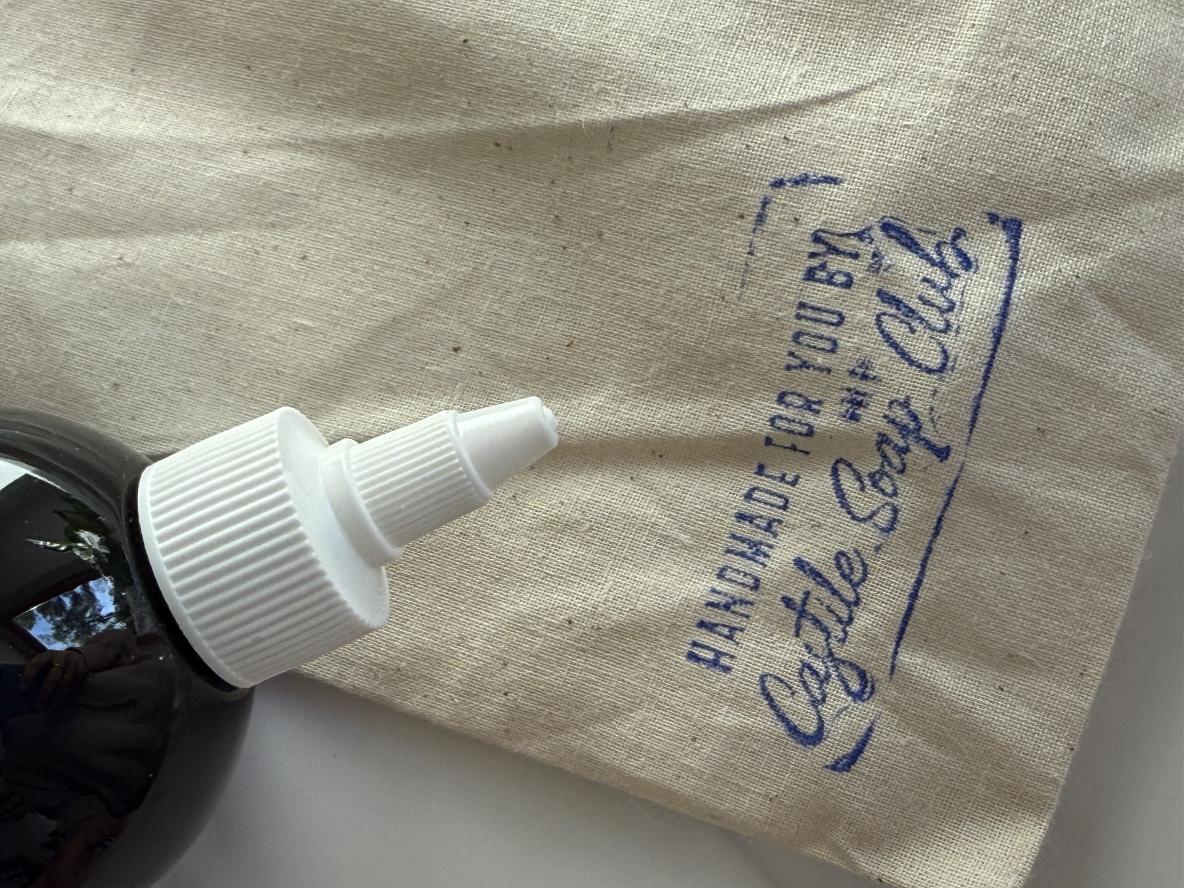 Close-up of a black bottle with a white nozzle on a bag labeled 'Castile Soap Club.'