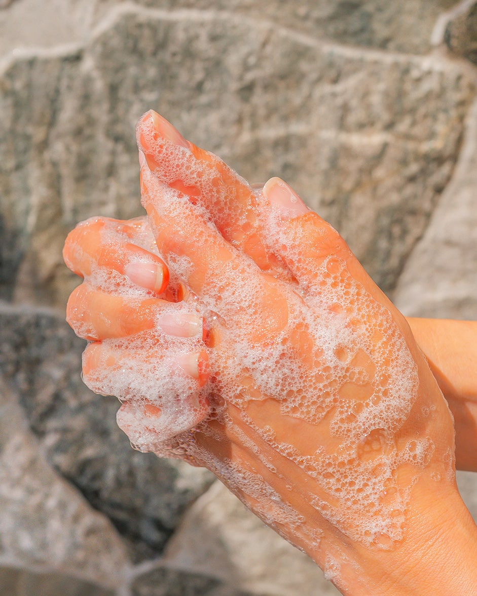 Hands covered in soap suds against a stone background.