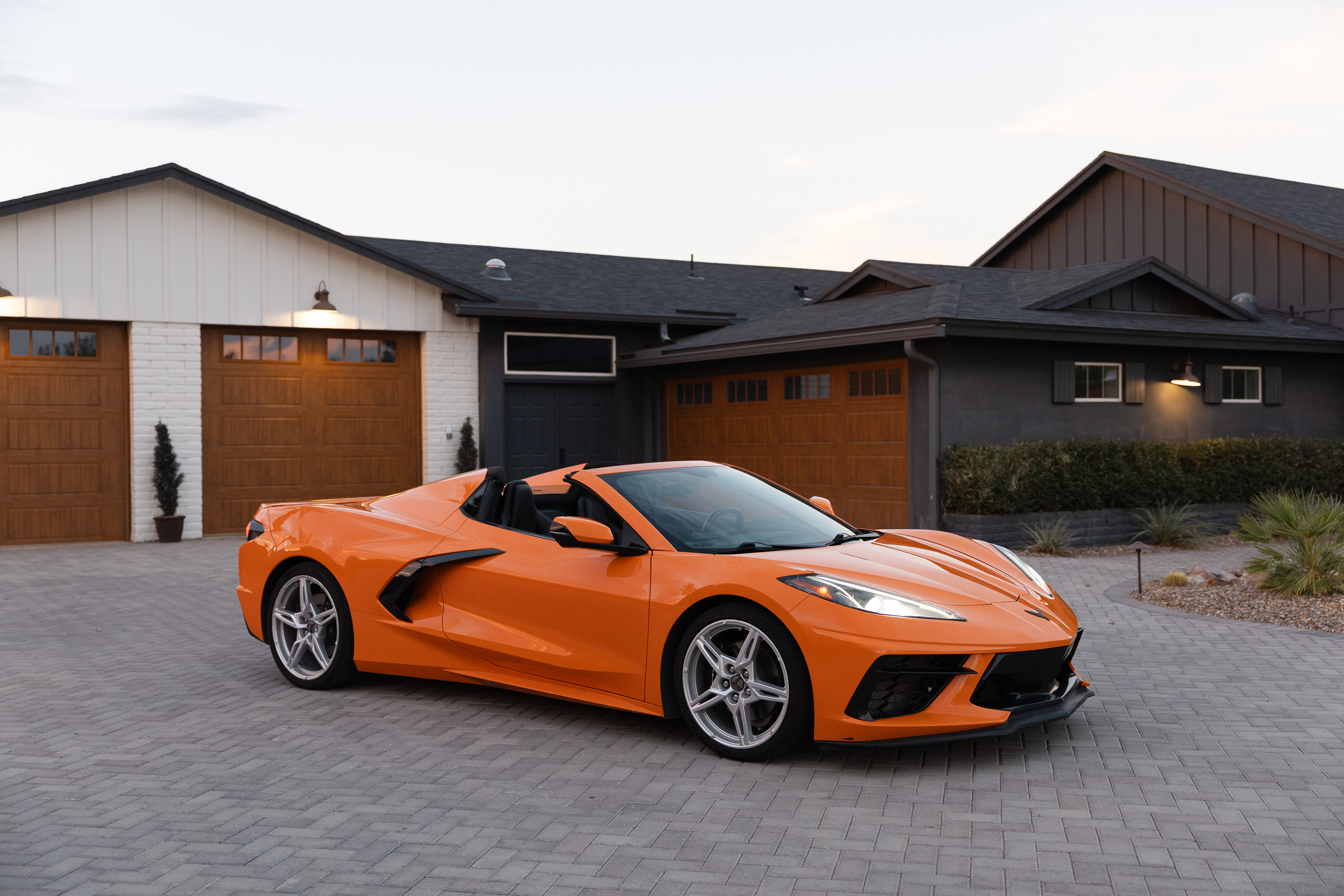 An orange convertible sports car parked on a paver driveway in front of a modern house.
