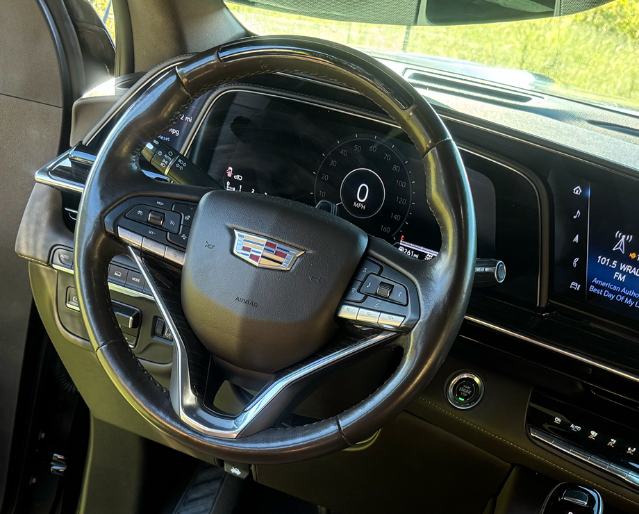 A close-up of the steering wheel and digital dashboard inside a modern Cadillac.