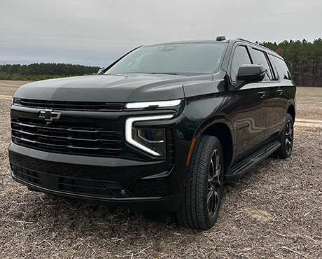 A black Chevrolet SUV is parked in a barren field under a cloudy sky.