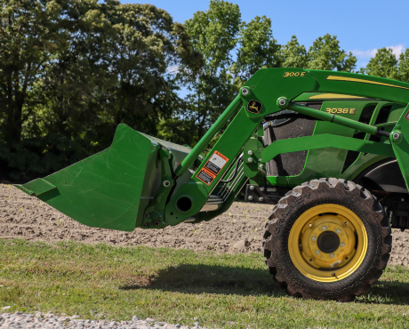 A close-up of the front loader bucket and wheel of a green John Deere tractor parked outdoors.