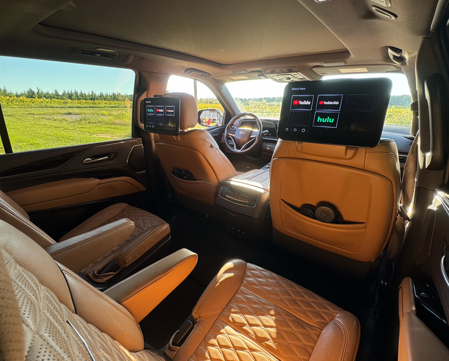 The spacious interior of an SUV with tan leather seats and screens on the headrests.