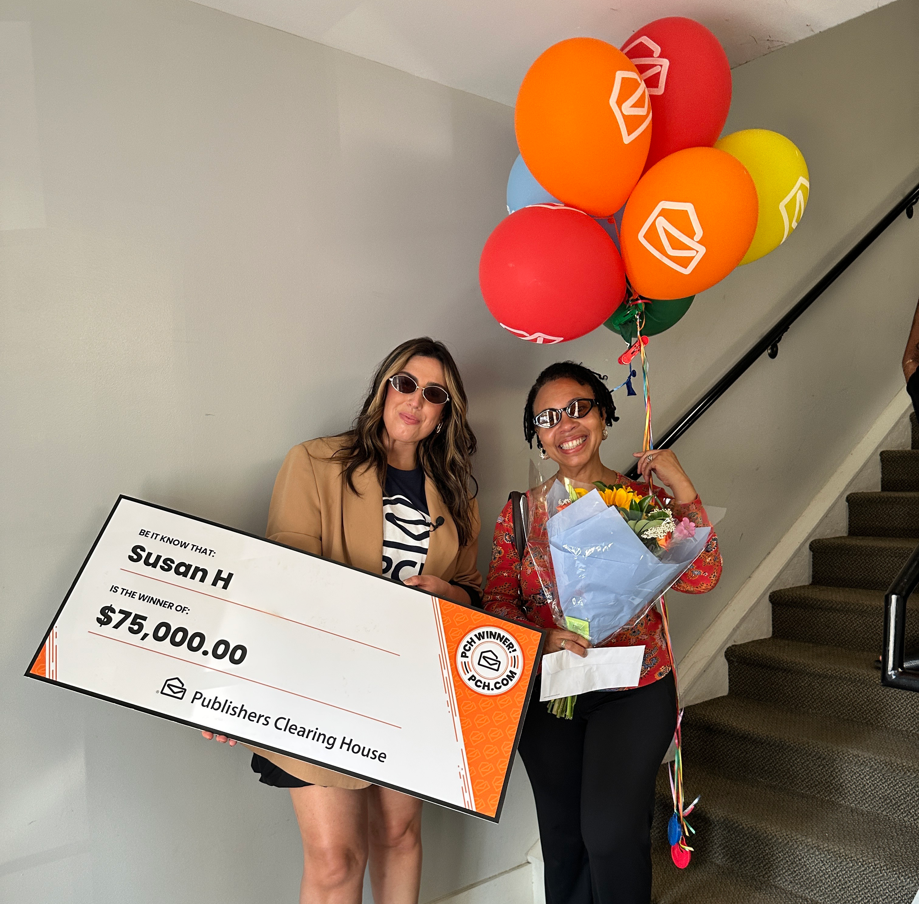 Two women pose with a large check for $75,000 from Publishers Clearing House, flowers, and balloons.
