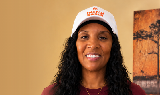 A smiling woman wears a white cap with orange text that reads, 'I'm a PCH Winner!'