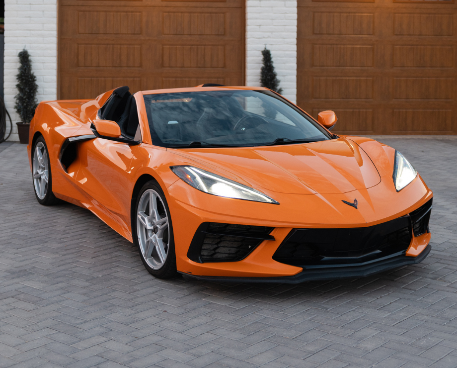 A close-up side view of a bright orange convertible sports car parked on a paved street.