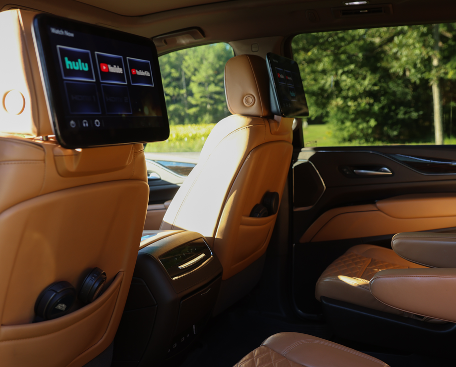 The interior of a vehicle with tan leather seats and rear entertainment screens on the headrests.